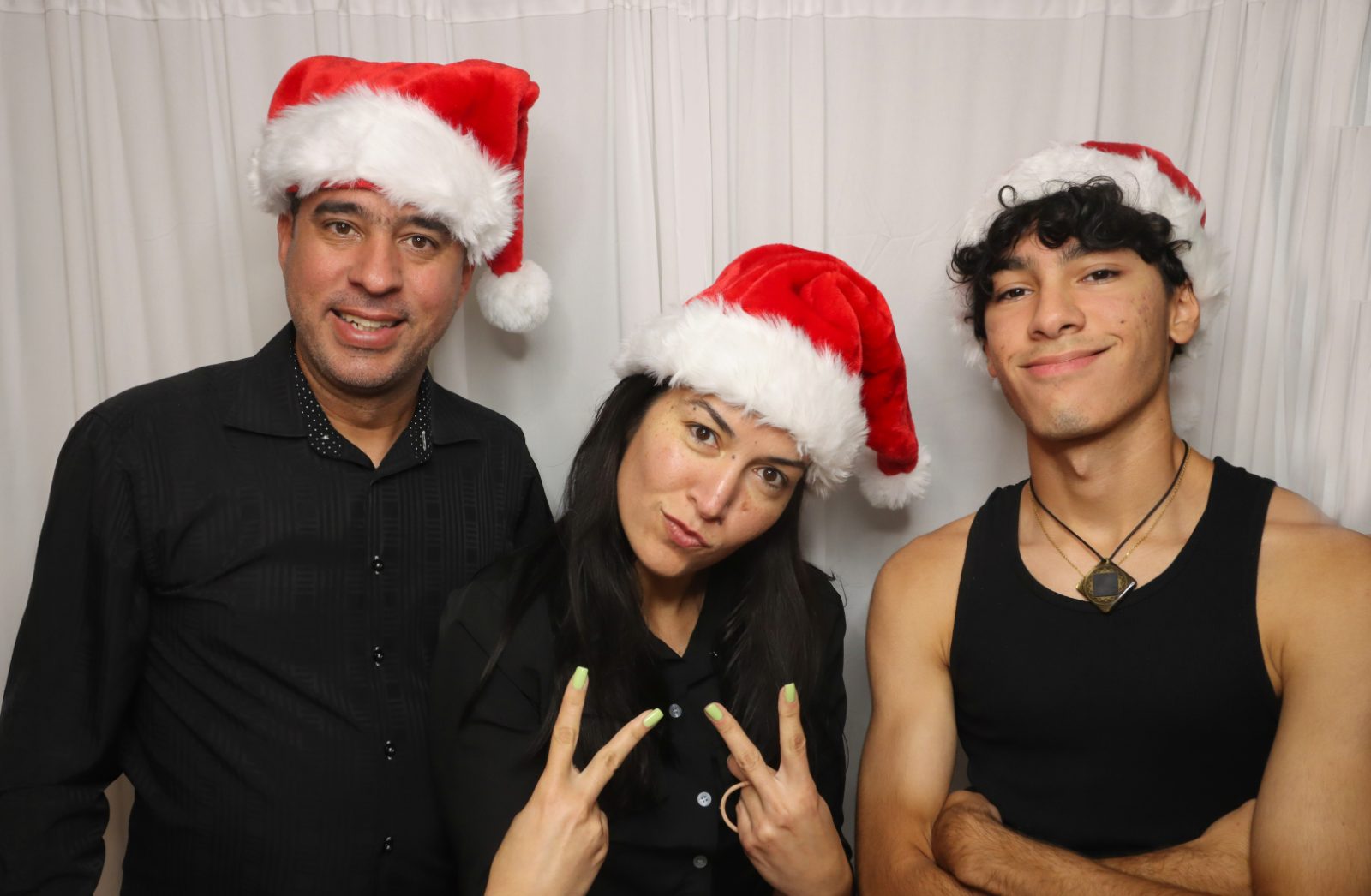 Family in Santa hats at a Kiko Booths photobooth with a white drape backdrop